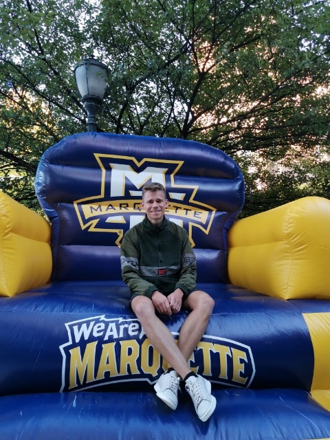 Tim Decker, a graduate student in the College of Business Administration, poses on a Marquette themed blow-up chair. Decker is a student from Berlin, Germany and produces music under the name Tim Yello.